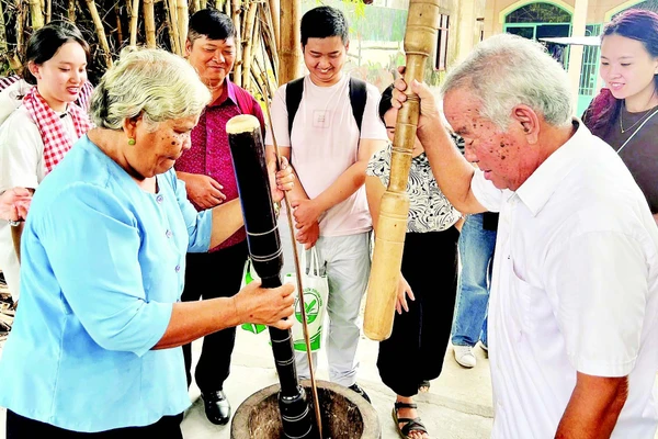 Vợ chồng ông Thạch Sang giã cốm dẹp cho khách du lịch xem.