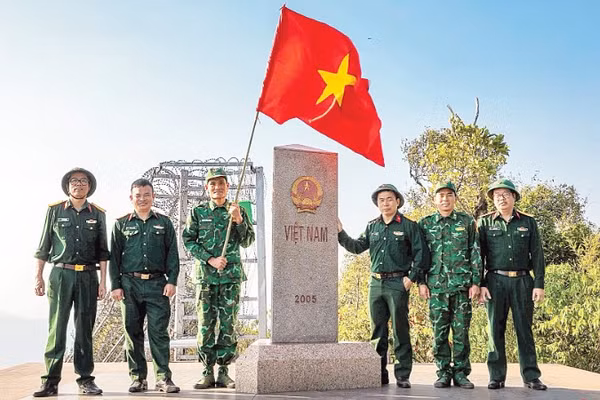 Thượng úy Lục Vĩnh Lương (người cầm cờ) cùng tác giả và đoàn công tác tại Cột mốc số 0 - Ngã ba biên giới A Pa Chải - Cực tây Tổ quốc.