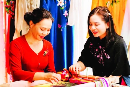 Nghệ nhân Nguyễn Thị Hằng (bên trái) giới thiệu kỹ thuật thêu trên lụa. (Ảnh: THÀNH NAM)