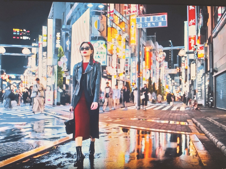 Ảnh chụp từ videoclip được tạo ra từ AI với câu lệnh mô tả một cô gái đang đi trên đường phố Nhật Bản với mái tóc nâu và nước da trắng, đeo kính.