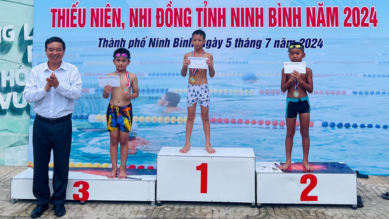 Ban tổ chức trao giải cho các vận động viên nam nội dung 25 m bơi ếch lứa tuổi 6-8.