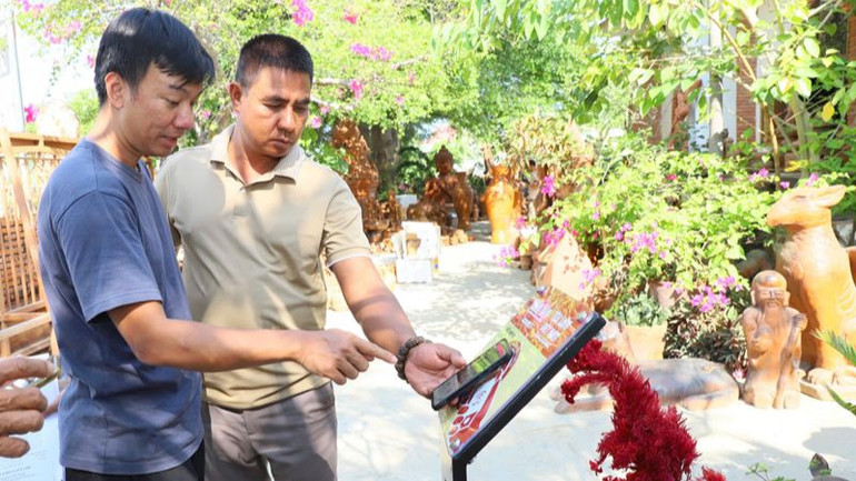 Kỹ thuật viên hướng dẫn người dân sử dụng điện thoại thông minh kết nối với bảng có công nghệ kết nối không dây tầm ngắn để tìm hiểu thông tin về các điểm du lịch tại Ninh Thuận, chọn nơi tham quan và trải nghiệm khi đến địa phương.