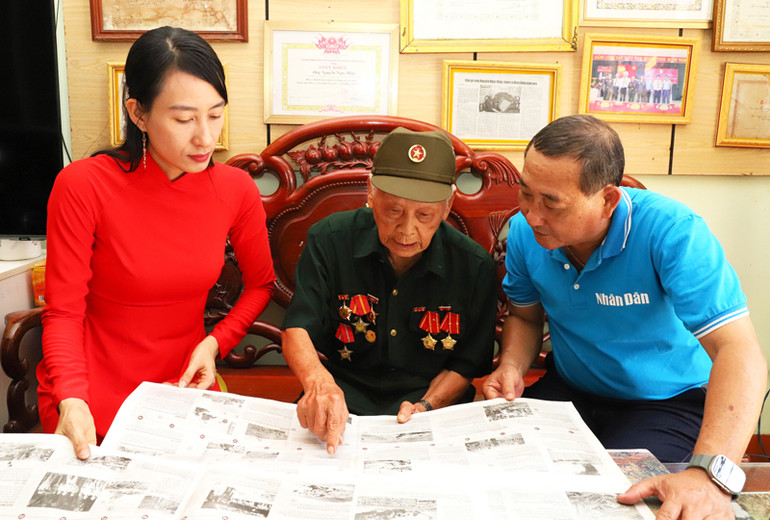 Cụ Nguyễn Ngọc Điệp chỉ tay vào ấn phẩm giới thiệu và kể lại diễn biến mà cụ đã cùng với đồng đội tấn công hỏa lực vào sào huyệt quân địch, góp phần vào chiến thắng của chiến dịch