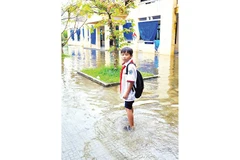 Mỗi khi trời mưa, nước dâng ngập đường, học sinh phải đi vòng, vào đến cổng trường lại phải lội nước trong sân để vào lớp. (Ảnh QUỐC CƯỜNG)
