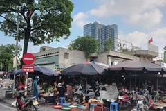 Các quầy, sạp bên trong chợ Ngã Tư Sở bị bỏ không, nhưng nhiều người dân lại tràn ra vỉa hè để bán hàng. (Ảnh VĂN HỌC) 