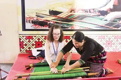 Nghệ nhân H’Bình giới thiệu cách dệt thổ cẩm dân tộc Mạ cho du khách nước ngoài đến tham quan tổ hợp tác.