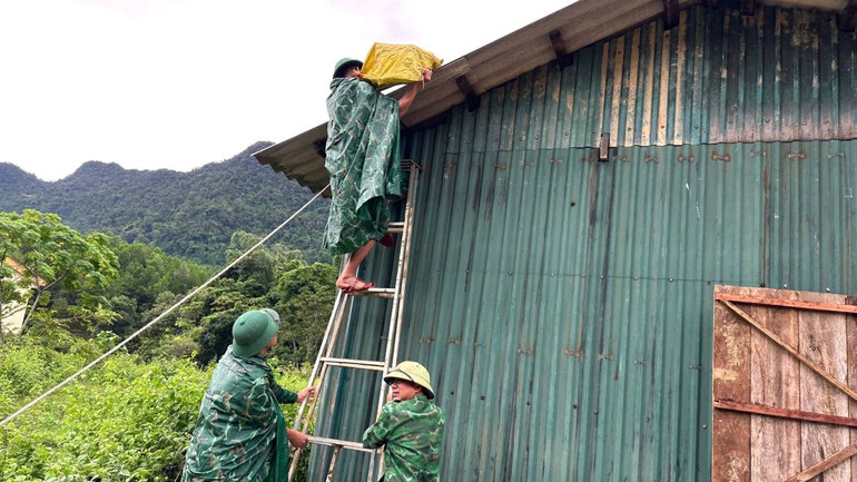 Cán bộ, chiến sĩ Đồn Biên phòng Cà Xèng giúp bà con người Rục ở xã Thượng Hóa, huyện Minh Hóa đặt các bao cát lên mái nhà đề phòng gió bão cuốn bay.
