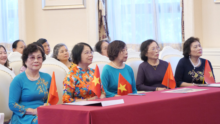 Các bác, các chị trong trang phục áo dài truyền thống cầm cờ Tổ quốc.