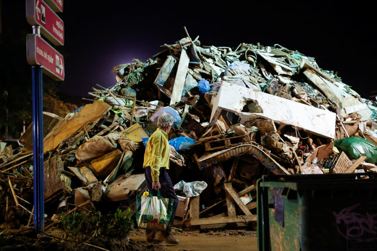 Một người đi bộ bên cạnh đống đổ nát phủ đầy bùn đất sau trận mưa lớn gây ra lũ lụt, ở Paiporta, gần Valencia. (Ảnh: Reuters)