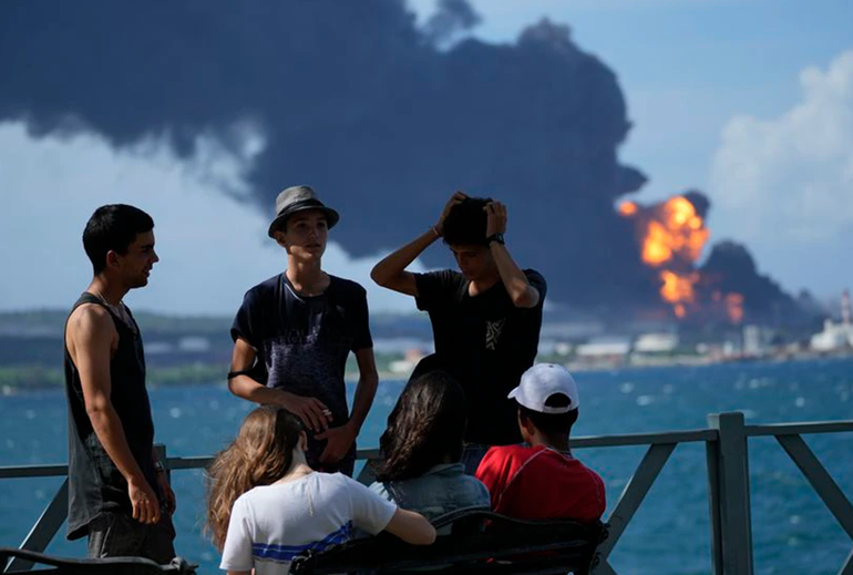 Nhóm thanh niên tụ tập trên một bến tàu trong khi lửa và khói vẫn tiếp tục bốc lên từ Căn cứ siêu tàu Matanzas. (Ảnh: AP)