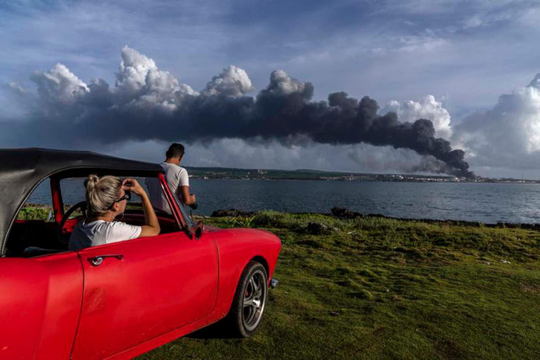 Ngọn lửa lan rộng ở thành phố Matanzas, cách thủ đô Havana 90km về phía đông, nơi có ít nhất 3 thùng dầu thô bốc cháy sau khi bị sét đánh vào đêm thứ 6 vừa qua. Trong ảnh, hai người dân quan sát thấy cột khói khổng lồ bốc lên từ kho nhiên liệu tại thành phố ven biển này. (Ảnh: AP)