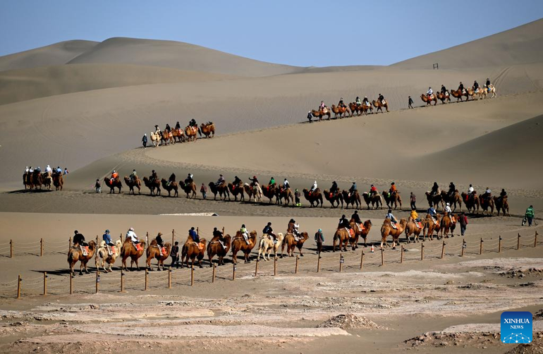 Du khách trải nghiệm cưỡi lạc đà trên cồn cát tại khu danh thắng núi cát Minh Sa và Nguyệt Nha Tuyền, thành phố Đôn Hoàng, tỉnh Cam Túc, ngày 5/4.