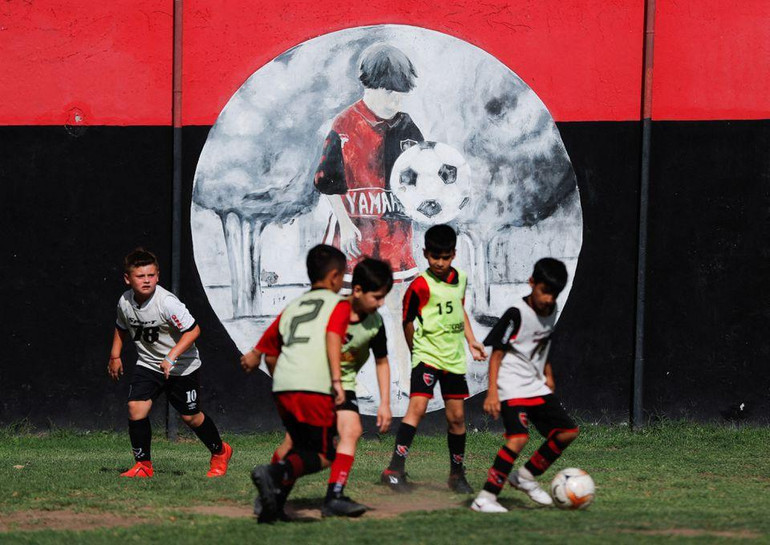 Các em nhỏ chơi bóng cạnh bức tranh tường về Messi trong trung tâm huấn luyện của câu lạc bộ Newell's Old Boys, đội bóng Messi đã từng chơi khi còn niên thiếu ở Rosario, Argentina. (Ảnh: Reuters)