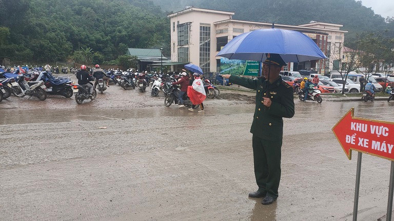 Cán bộ đồn Biên phòng cửa khẩu quốc tế Nậm Cắn đội mưa hướng dẫn người dân ra, vào chợ.