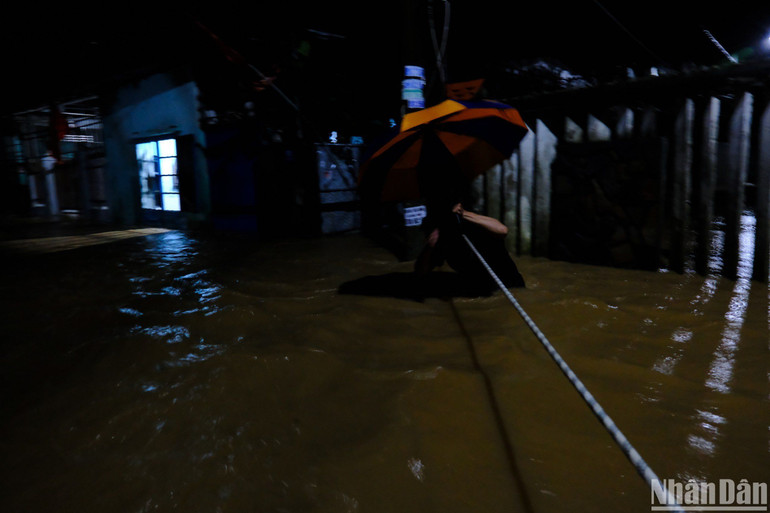 Người dân bám vào dây để di chuyển an toàn qua khu vực ngập gần 1m. (Ảnh: ANH ĐÀO)