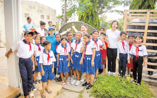 Chị Nguyễn Hồng Hạnh, cán bộ nước sạch, vệ sinh môi trường - UNICEF Việt Nam (áo xanh, bên trái) và cán bộ Masterise Group chia sẻ niềm vui với các em học sinh Trường tiểu học Long Phú C khi đón thiết bị nhà vệ sinh không phát thải.