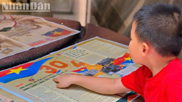 Một cháu nhỏ với tương tác với phụ san đặc biệt của Báo Nhân Dân kỷ niệm 50 năm Ngày giải phóng miền nam, thống nhất đất nước.