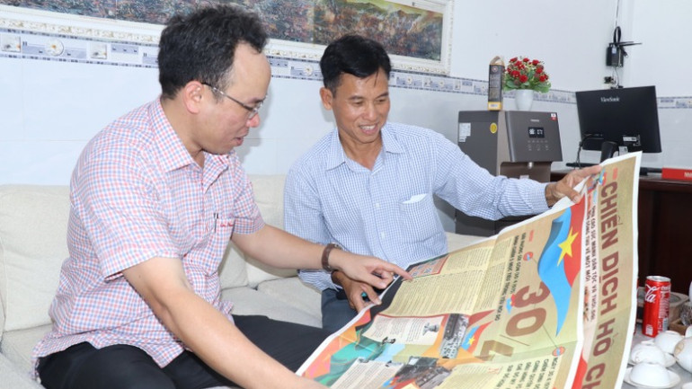 Anh Nguyễn Ngọc Tuấn (bên phải) tìm hiểu thông tin trên phụ san đặc biệt Báo Nhân Dân.