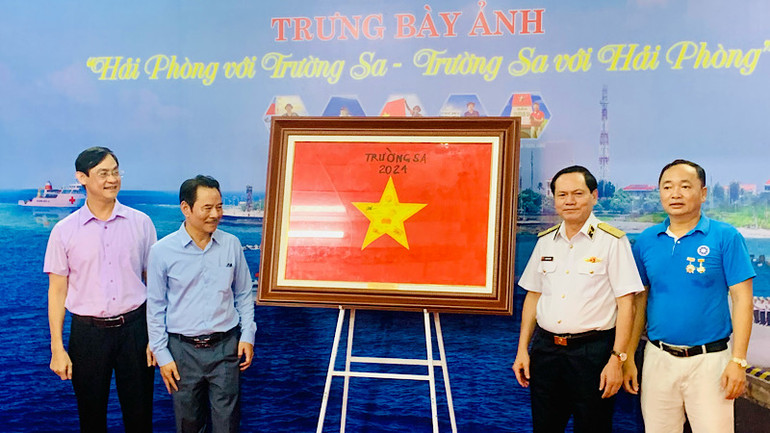 Chuẩn đô đốc Phạm Văn Luyện, Phó chủ nhiệm Chính trị Quân chủng Hải quân và nhà nhiếp ảnh Đỗ Trọng Luân trao cờ Tổ quốc có nhiều chữ ký của lãnh đạo các đảo ở Trường Sa và Nhà giàn DK tặng Hội Nhà báo thành phố Hải Phòng.