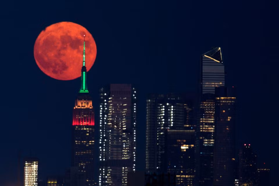 Trăng tròn màu cam đỏ mọc sau Tòa nhà Empire State ở thành phố New York, Mỹ tối 23/7. Ảnh: Reuters.