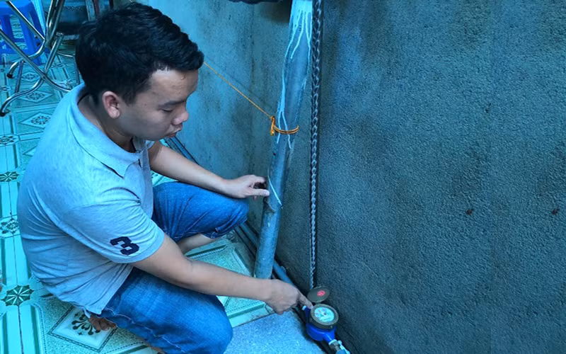 Anh Lương Chí Quang bên đường ống nước máy của gia đình.