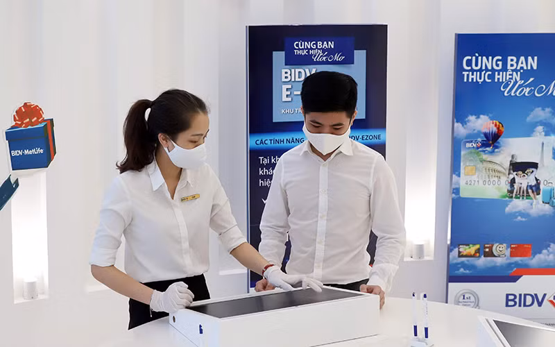 Nhân viên ngân hàng hướng dẫn khách hàng thực hiện các giao dịch tự động BIDV Ezone. Ảnh: MINH HÀ 