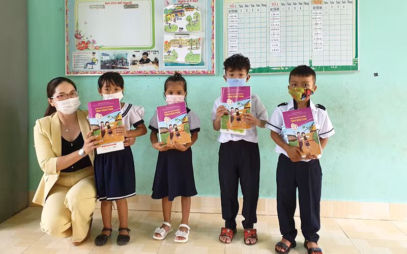 Cô Doãn Kim Huế, Hiệu trường Trường Tiểu học Cao Bá Quát trao sách giáo dục địa phương và tập vở do Báo Nhân Dân vận động cho các em học sinh. (Ảnh: Phúc Thắng)