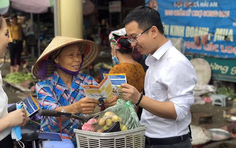 Người dân được phát tờ rơi và tư vấn về chính sách BHXH, BHYT. Ảnh: TÂM TRUNG.