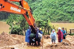 Các thầy, cô giáo ở xã Phước Chánh phải ngồi trên gàu của xe múc để vượt qua chỗ sạt lở vào trường học. (Ảnh: ANH QUÂN)