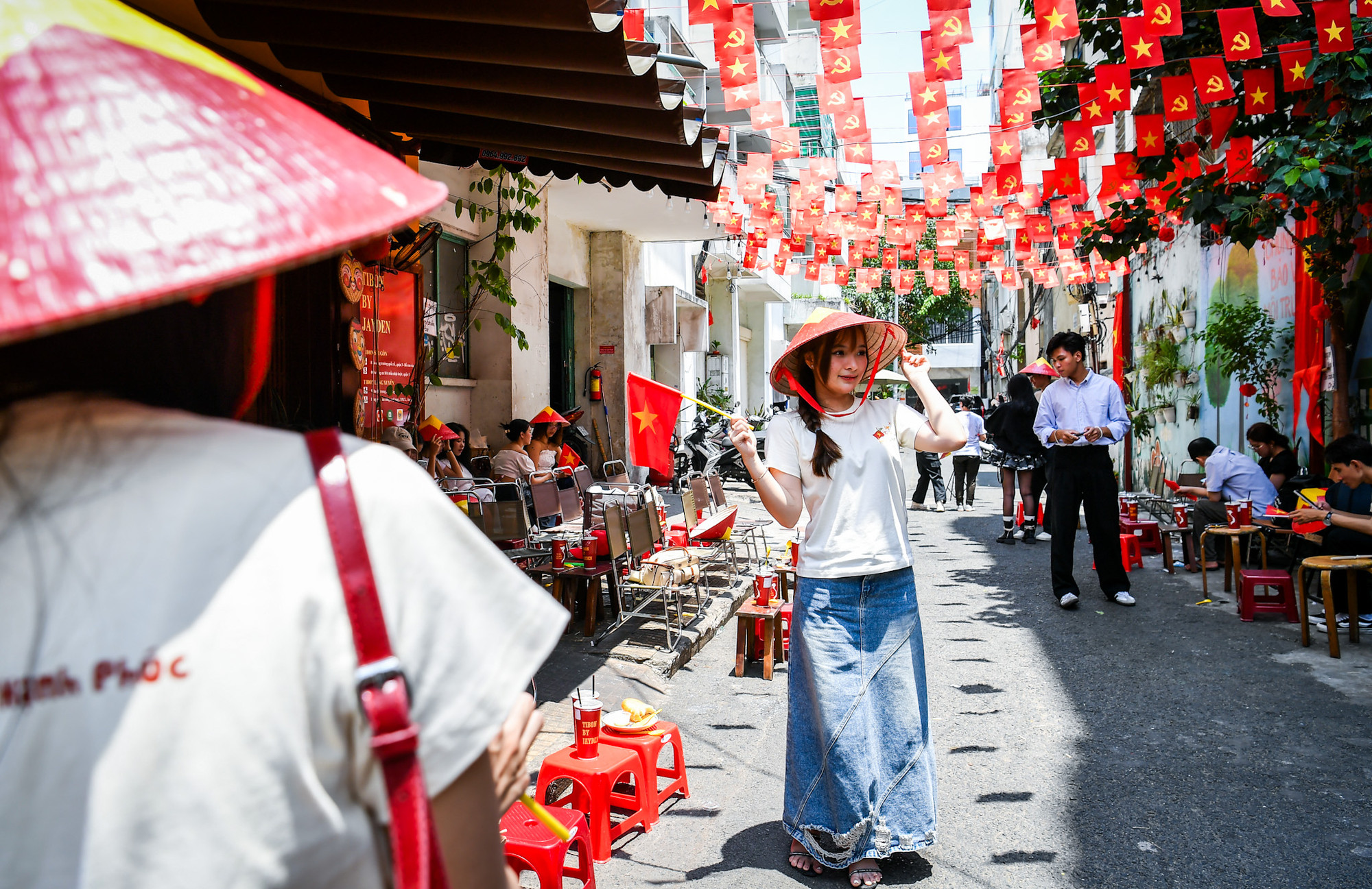 Cô gái trẻ tạo dáng trước dãy quán cà-phê rợp trời cờ hoa.