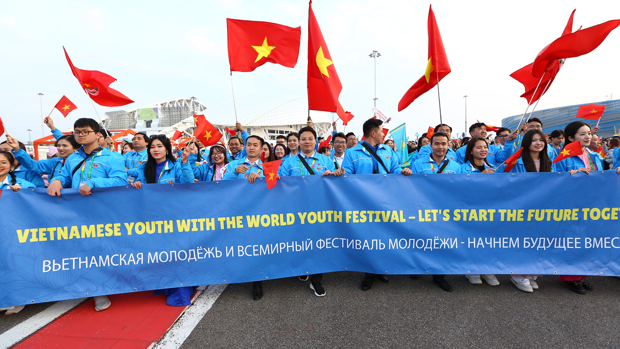Đoàn đại biểu Việt Nam mặc áo xanh Đoàn Thanh niên Cộng sản Hồ Chí Minh, mang theo cờ đỏ sao vàng, ảnh Chủ tịch Hồ Chí Minh, lá cờ Đoàn cùng băng rôn in thông điệp đoàn kết cùng xây dựng tương lai.