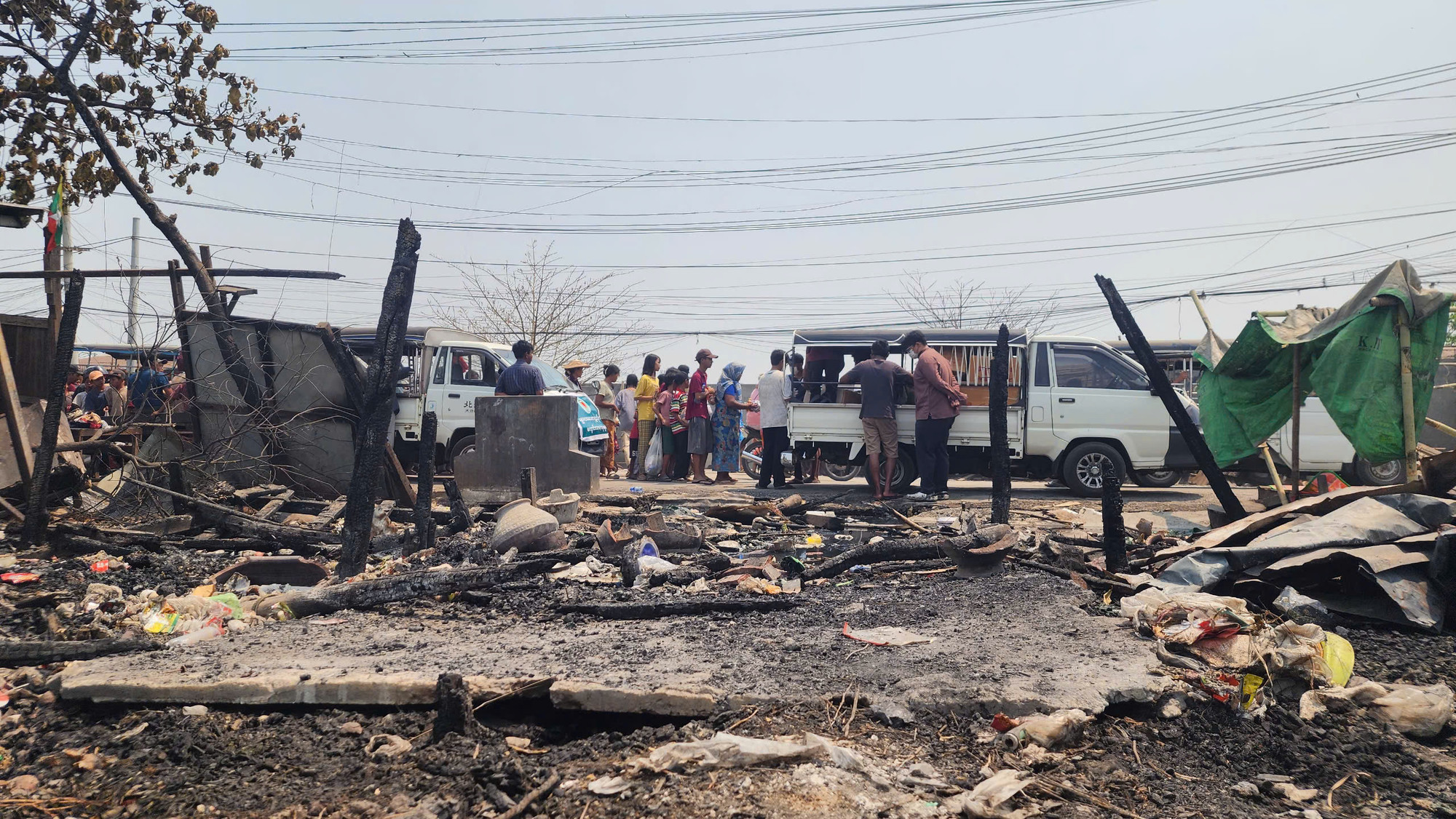Bên ngoài bãi đất đen đúa vốn là nhà của hàng nghìn người, hai chiếc xe ô-tô đỗ lại để phát đồ ăn trưa, nước uống cho các nạn nhân đã không còn nơi ở...