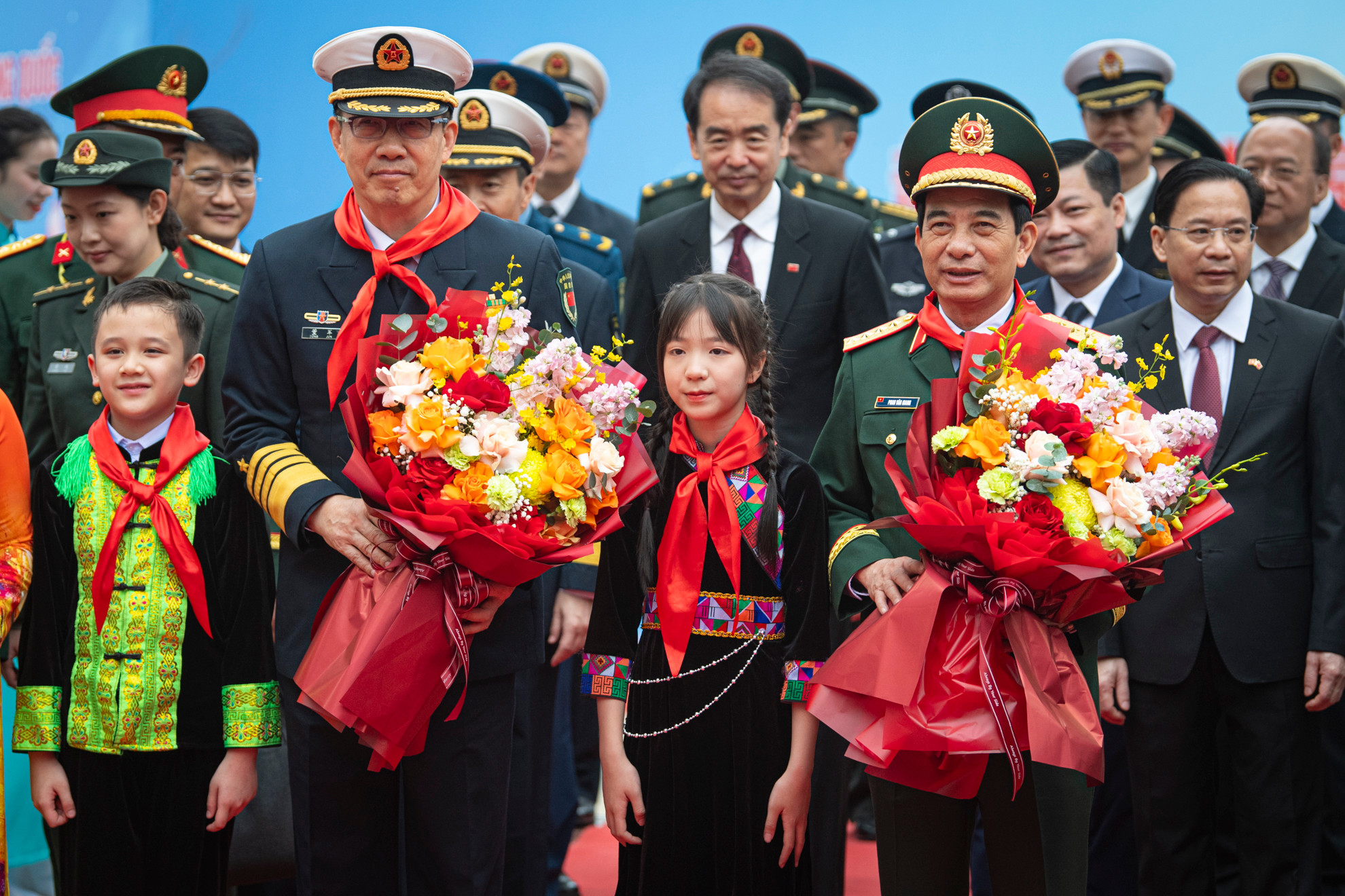 Các em học sinh đeo khăn quàng đỏ và tặng hoa hai Bộ trưởng.