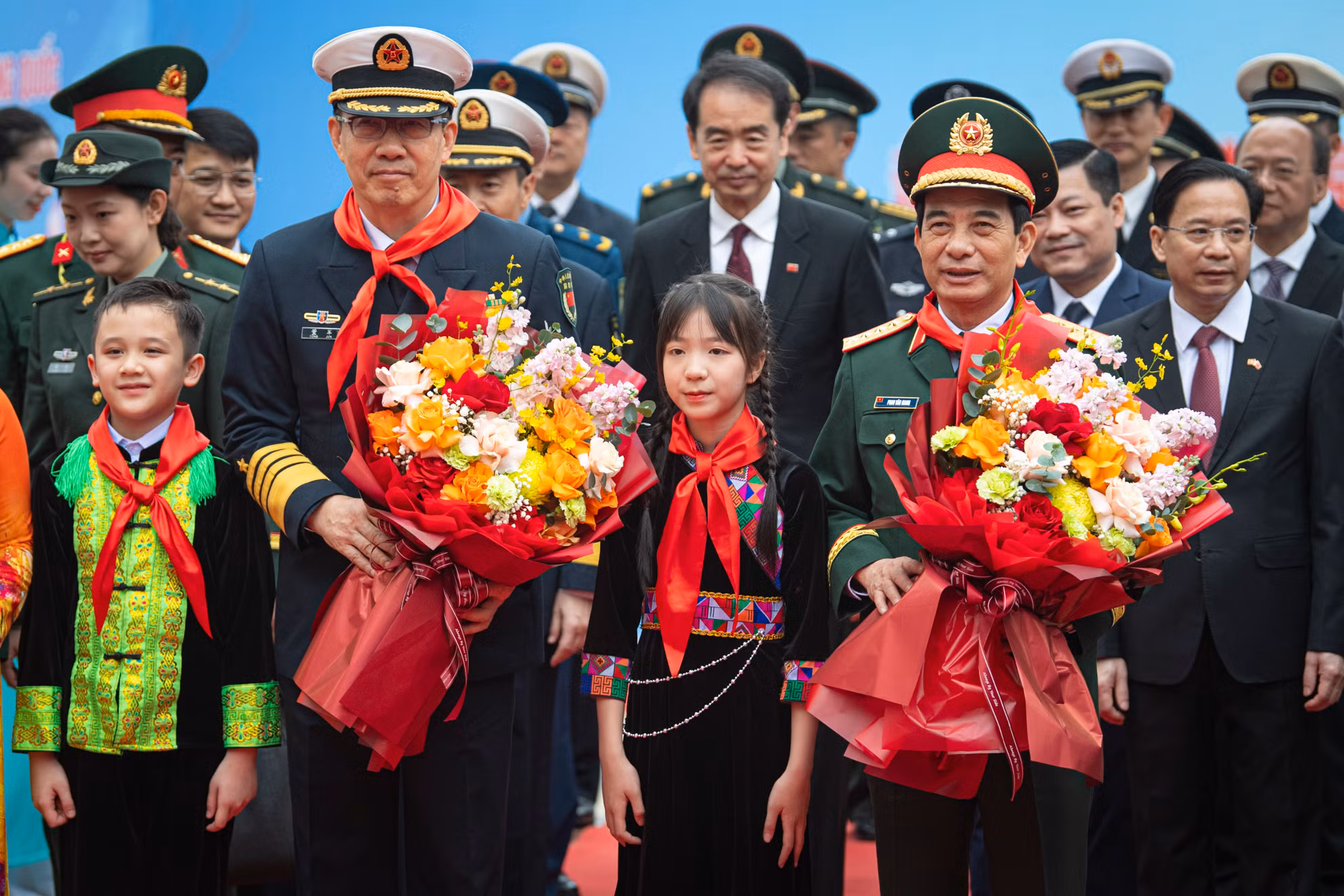 Các em học sinh đeo khăn quàng đỏ và tặng hoa hai Bộ trưởng.