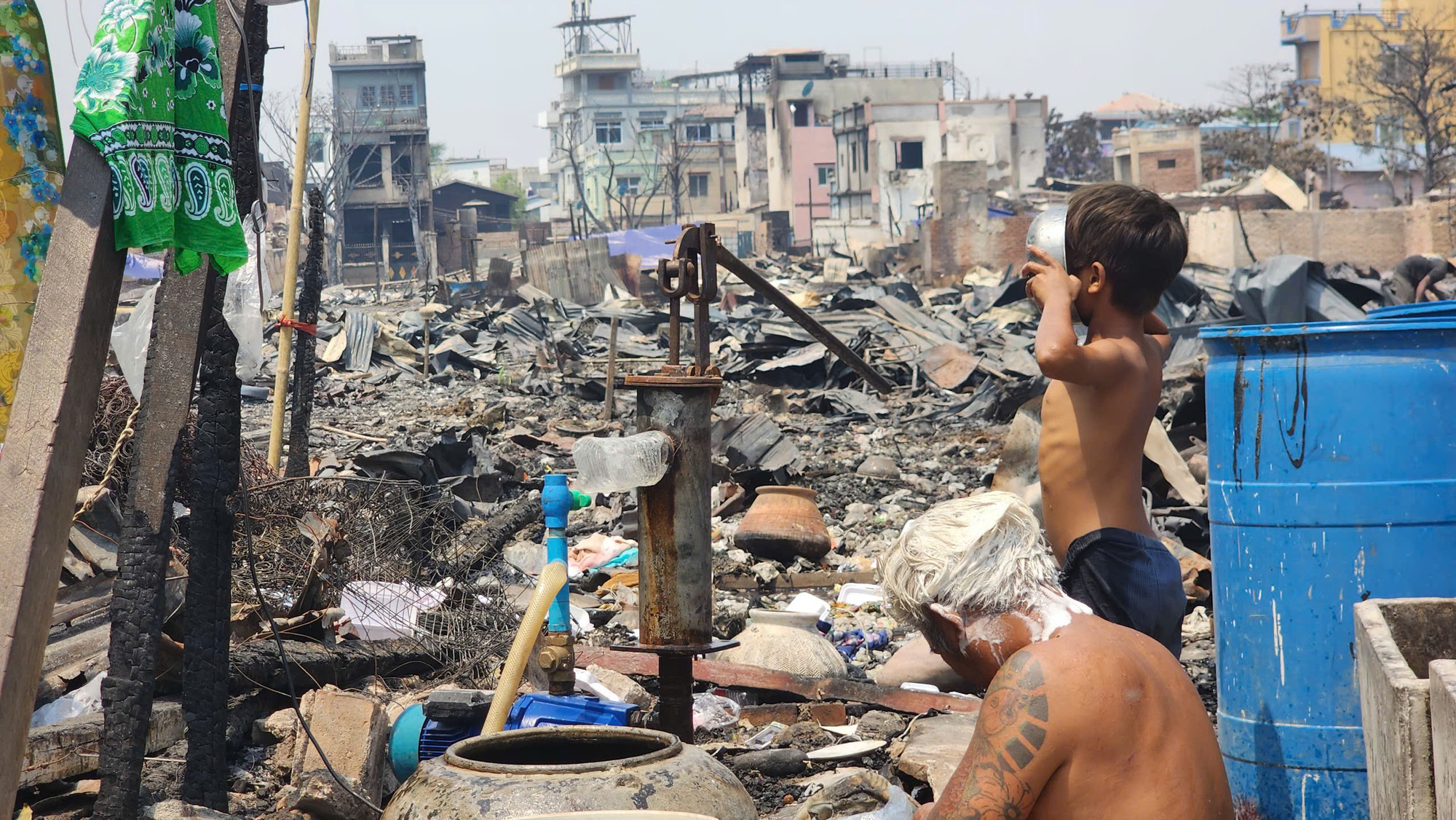 Một cậu bé uống nước tại giếng khoan. Phía sau lưng là dãy nhà gặp hỏa hoạn khi động đất tấn công.