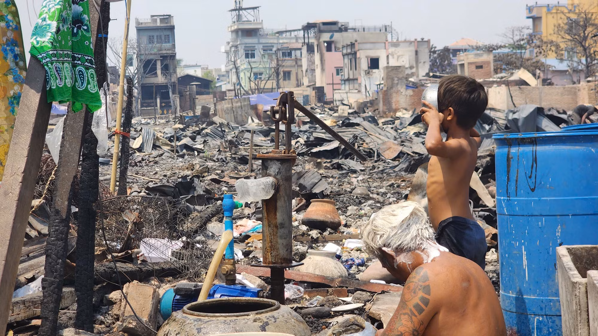 Một cậu bé uống nước tại giếng khoan. Phía sau lưng là dãy nhà gặp hỏa hoạn khi động đất tấn công. Một cậu bé uống nước tại giếng khoan. Phía sau lưng là dãy nhà gặp hỏa hoạn khi động đất tấn công.
