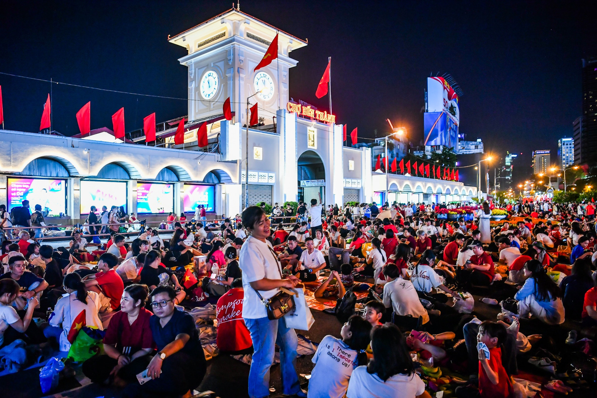 Gần 0 giờ đêm, khu vực Chợ Bến Thành vẫn như một ngày hội lớn. Hàng trăm người đã ngồi kín phía trước để trắng đêm đợi Lễ diễu binh, diễu hành sẽ diễn ra vào sáng 30/4.