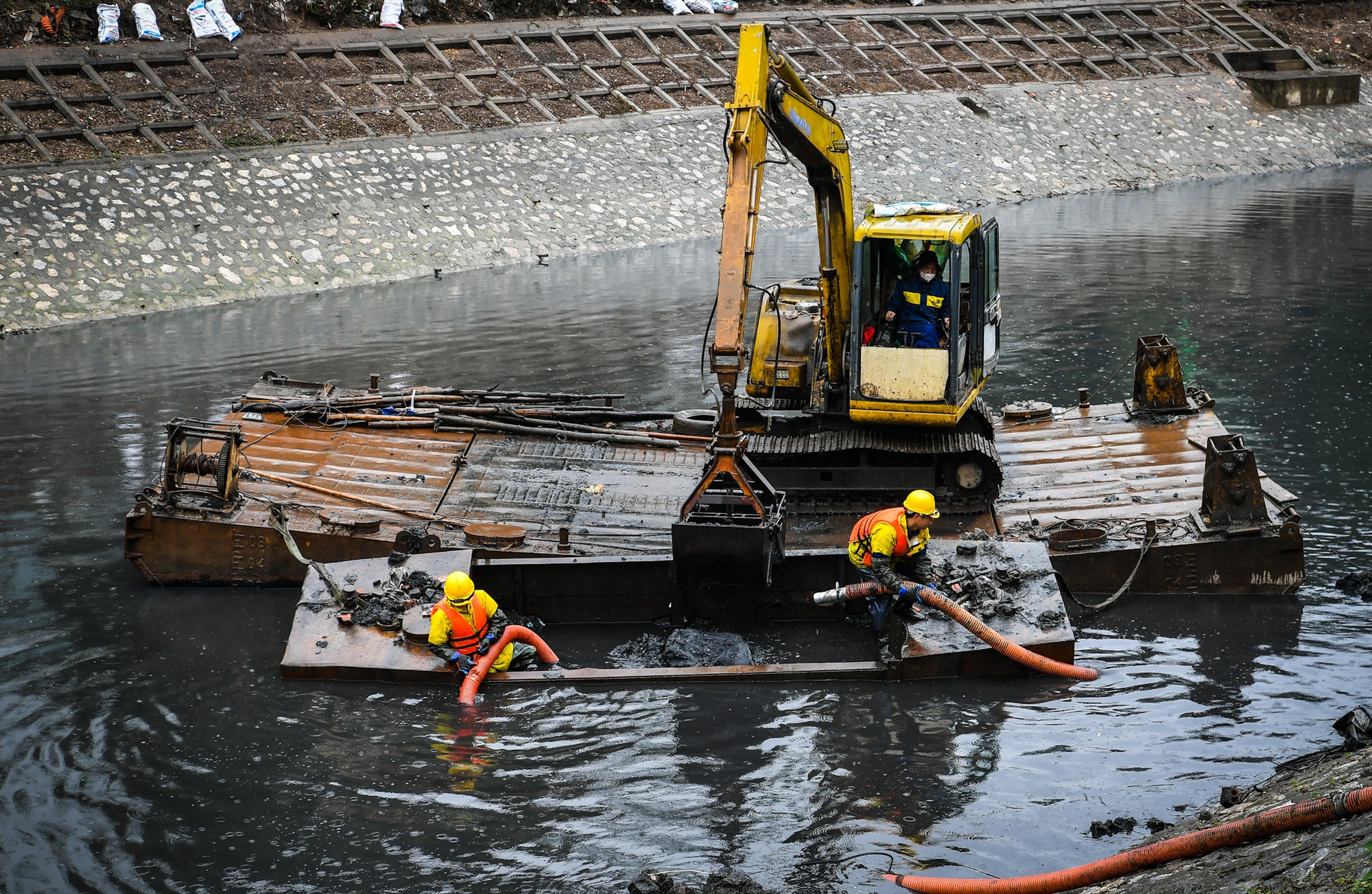 Ca làm việc hôm nay, tổ "đứng ống" bao gồm các anh Hoàng Tiến Nhất và Đinh Quang Huy. Do yêu cầu đặc thù, các anh phải ngâm mình trong thùng chứa cạnh bè nổi để xử lý bùn thải. Ngoài trời, mưa vẫn lất phất bay. Nhiệt độ hạ xuống chỉ còn trên 10 độ. Hơi bùn căm căm lùa vào sâu trong lớp áo quần bảo hộ.