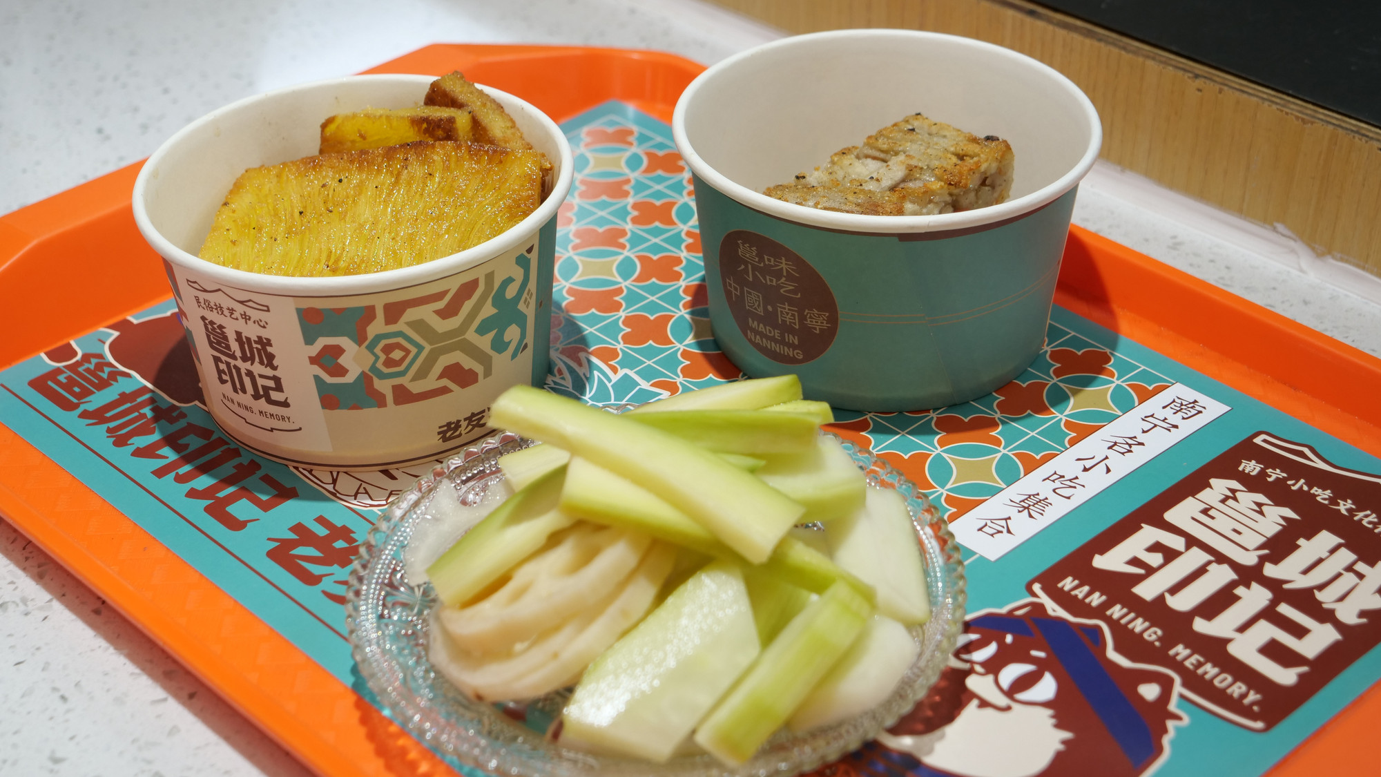 Món ăn vặt đặt trong cốc giấy và khay được thiết kế hoa văn trang nhã.