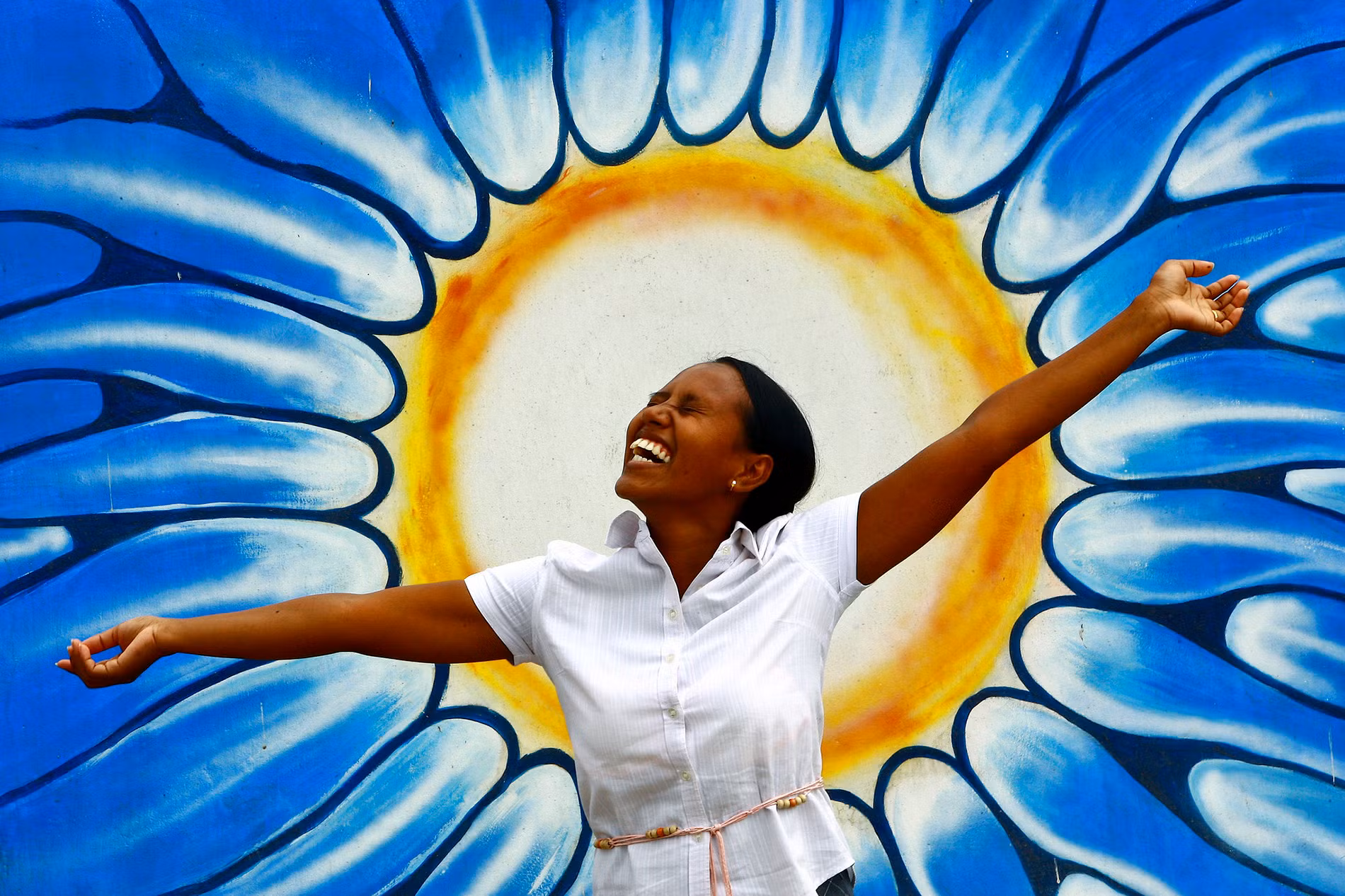 Người phụ nữ tạo dáng trước bức vẽ graffiti tượng trưng cho mặt trời nhân kỷ niệm Ngày Sức khỏe tâm thần thế giới.