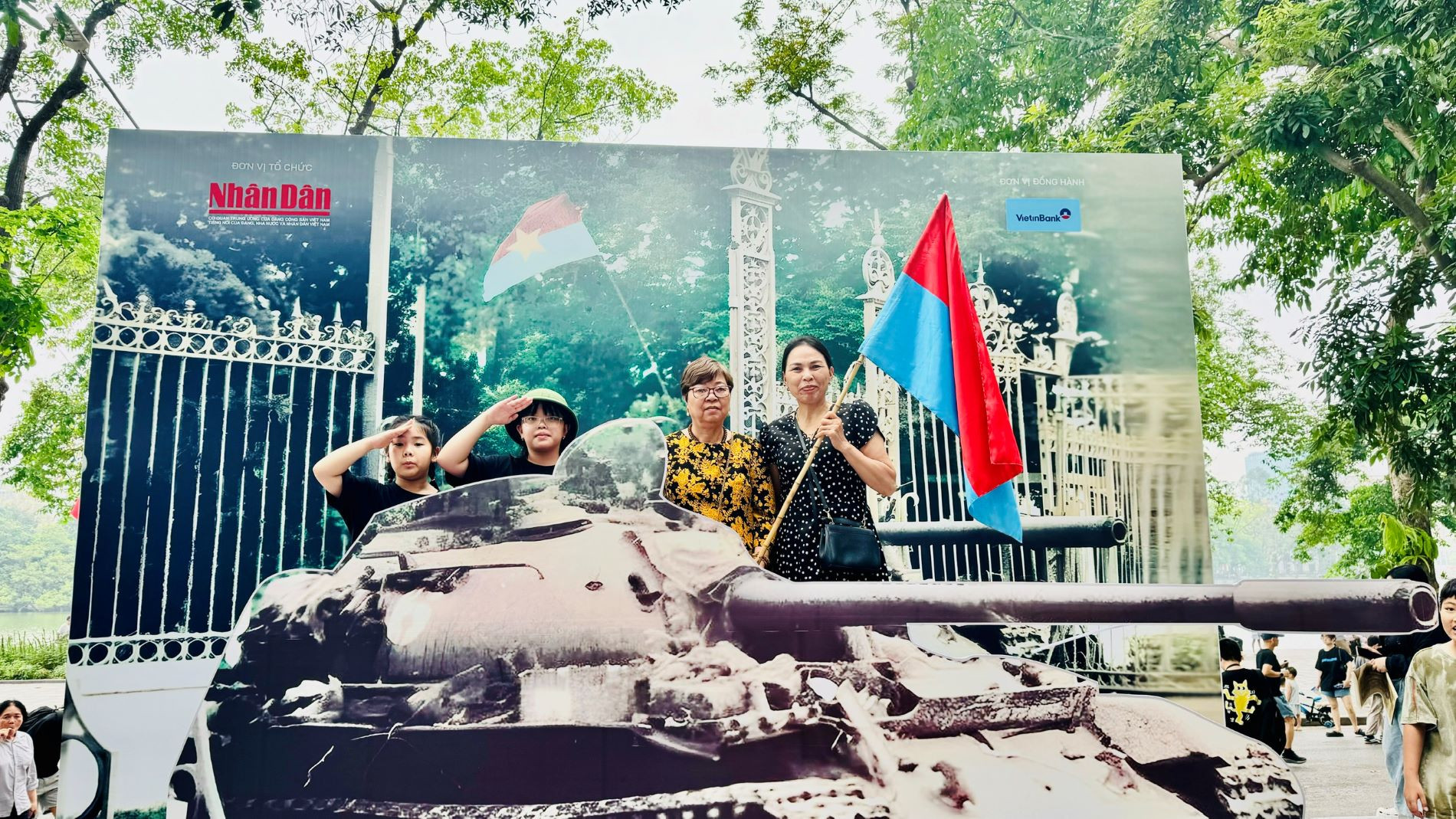 Bà Vương Thị Bình (cầm cờ) cùng người thân trong gia đình chụp ảnh tại mô hình xe tăng. (Ảnh: HNV) Bà Vương Thị Bình (cầm cờ) cùng người thân trong gia đình chụp ảnh tại mô hình xe tăng. (Ảnh: HNV)