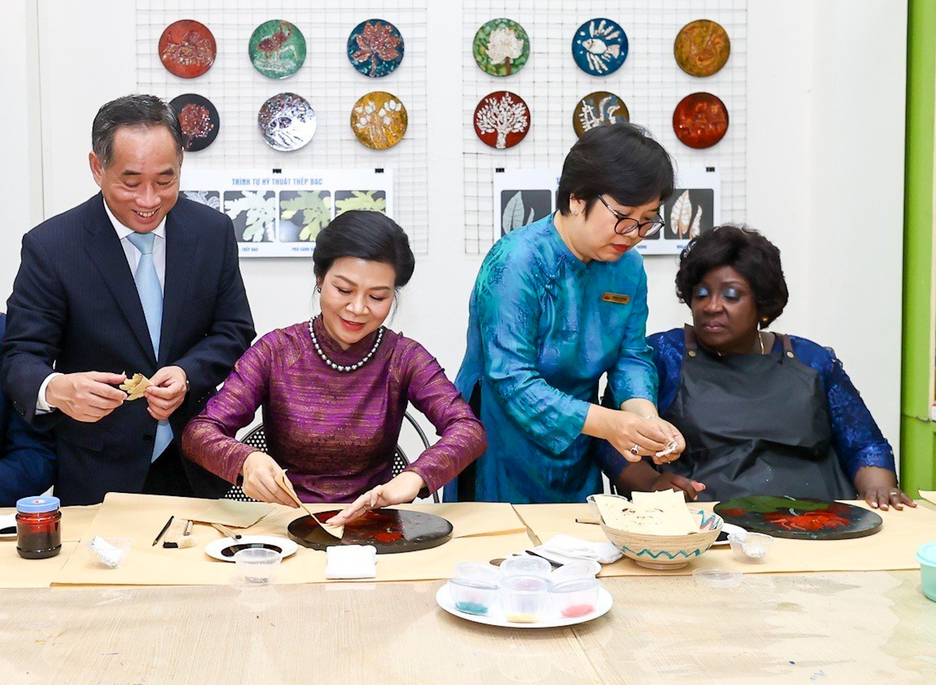 Hai Phu nhân nghe giới thiệu quá trình sáng tác tranh sơn mài và trải nghiệm dán bạc trên tranh.
