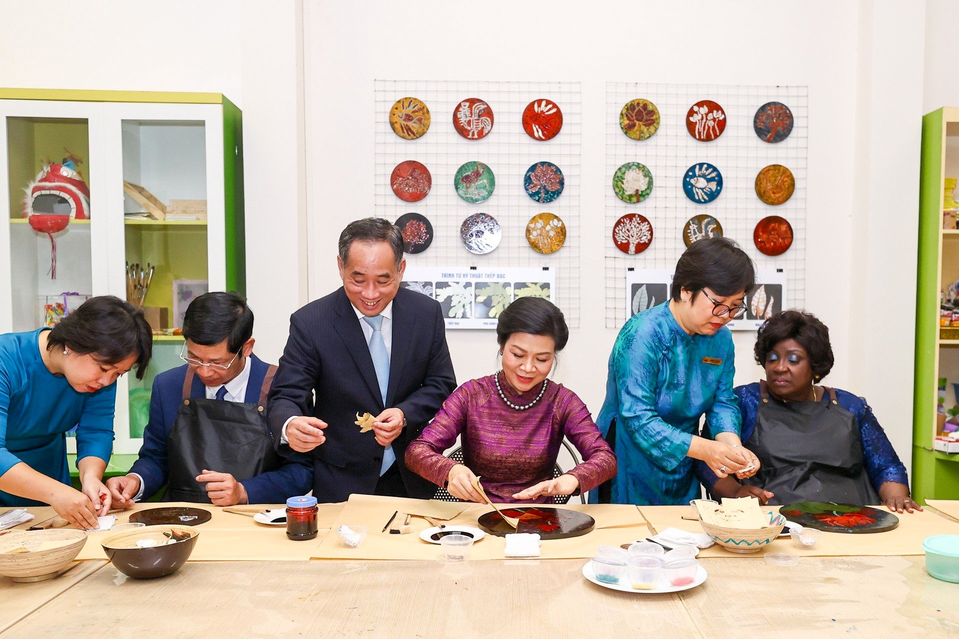 Hai Phu nhân nghe giới thiệu quá trình sáng tác tranh sơn mài và trải nghiệm dán bạc trên tranh.