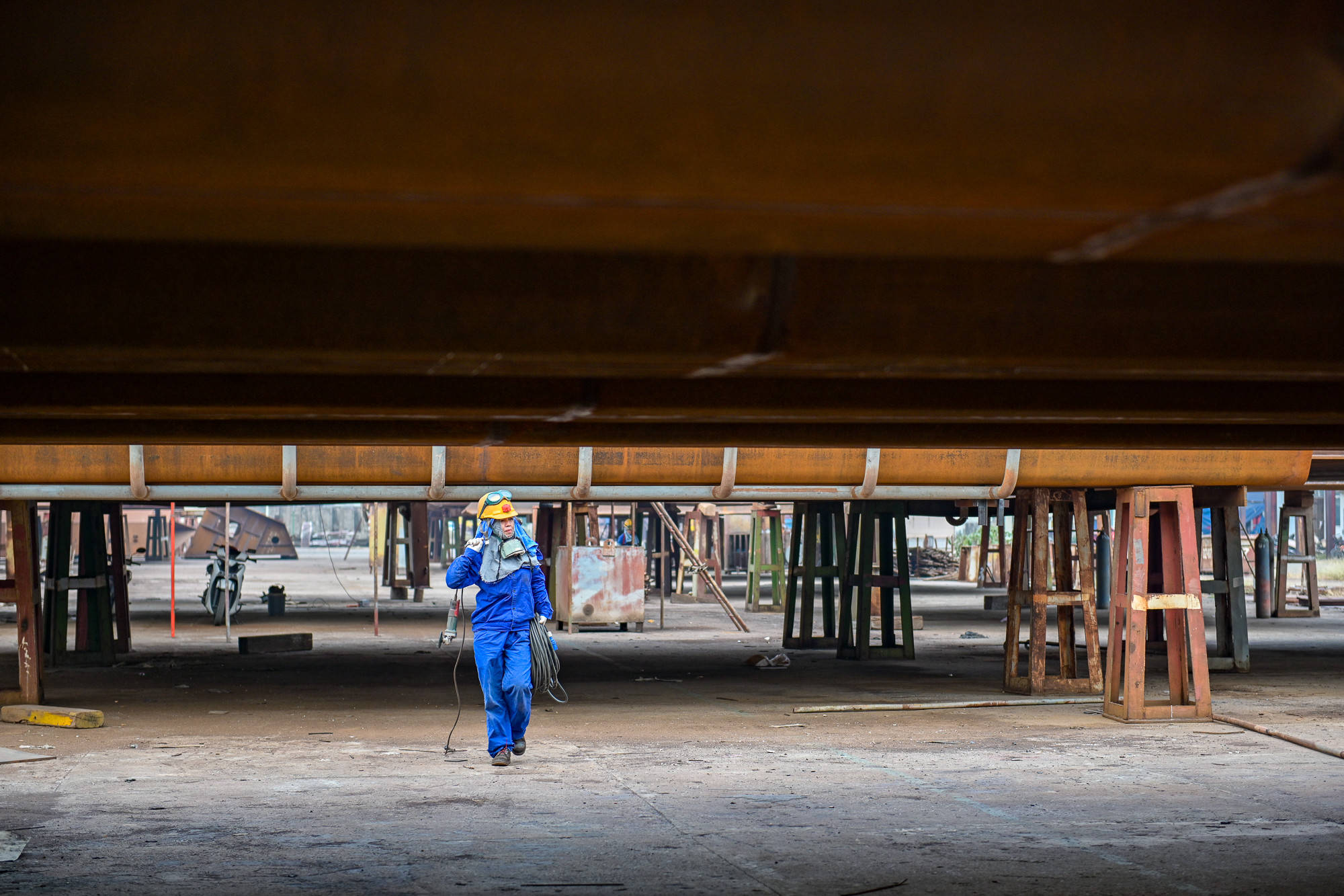 Chị Vũ Thị Cúc, tổ lắp ráp số 1, phân xưởng Vỏ tàu, thợ bậc 3/5 vác dây kéo điện đi giữa những block vỏ tàu khổng lồ, chuẩn bị bắt đầu ca trực mới kéo dài đến tối muộn. Chị Vũ Thị Cúc, tổ lắp ráp số 1, phân xưởng Vỏ tàu, thợ bậc 3/5 vác dây kéo điện đi giữa những block vỏ tàu khổng lồ, chuẩn bị bắt đầu ca trực mới kéo dài đến tối muộn.