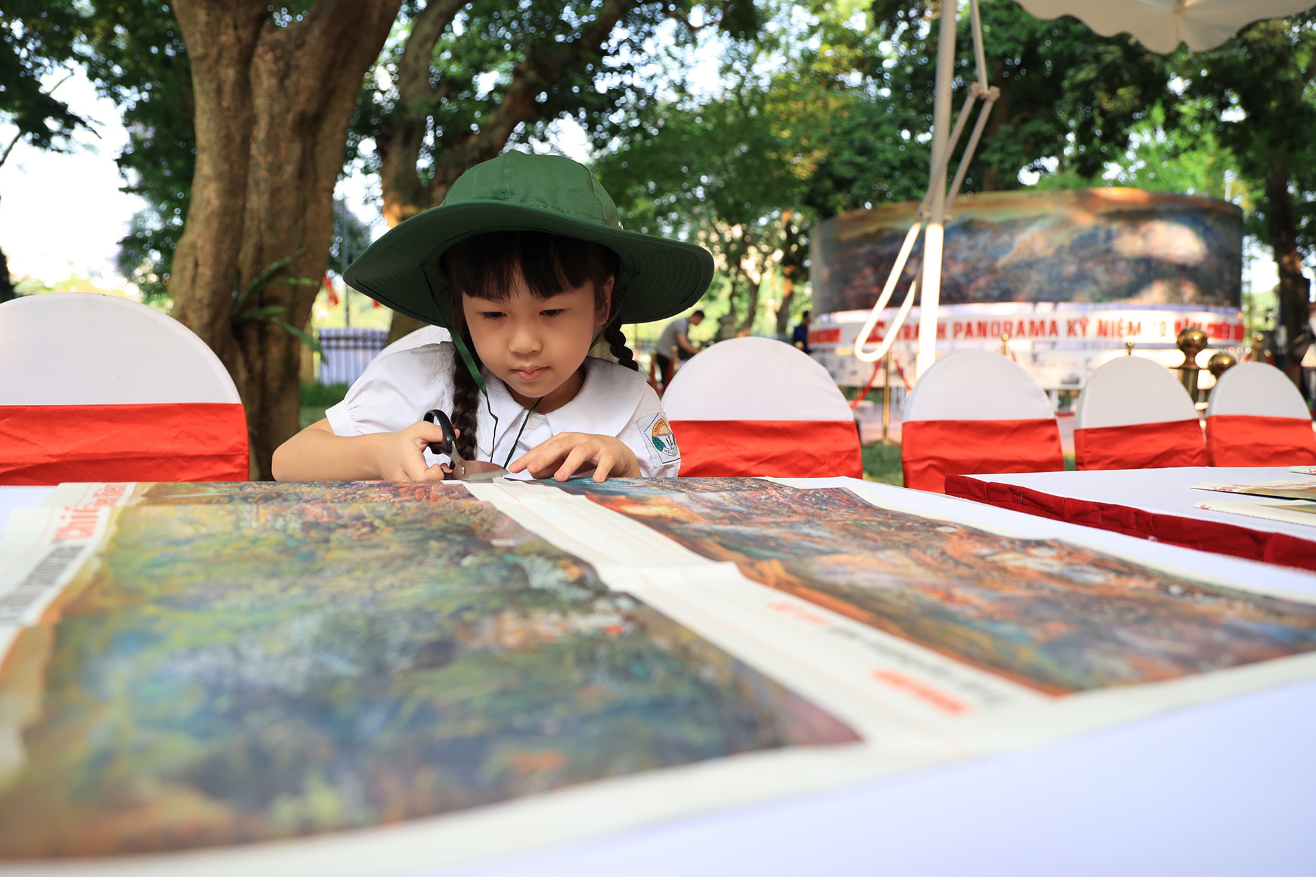 Tại Lễ khai mạc, Báo Nhân Dân đã tặng phụ trương đặc biệt kỷ niệm Chiến thắng Điện Biên Phủ cho khách tham quan tại cả hai địa điểm triển lãm ở Hà Nội và Điện Biên. Trong ảnh: Em bé chăm chú cắt dán tranh panorama “Chiến dịch Điện Biên Phủ”.