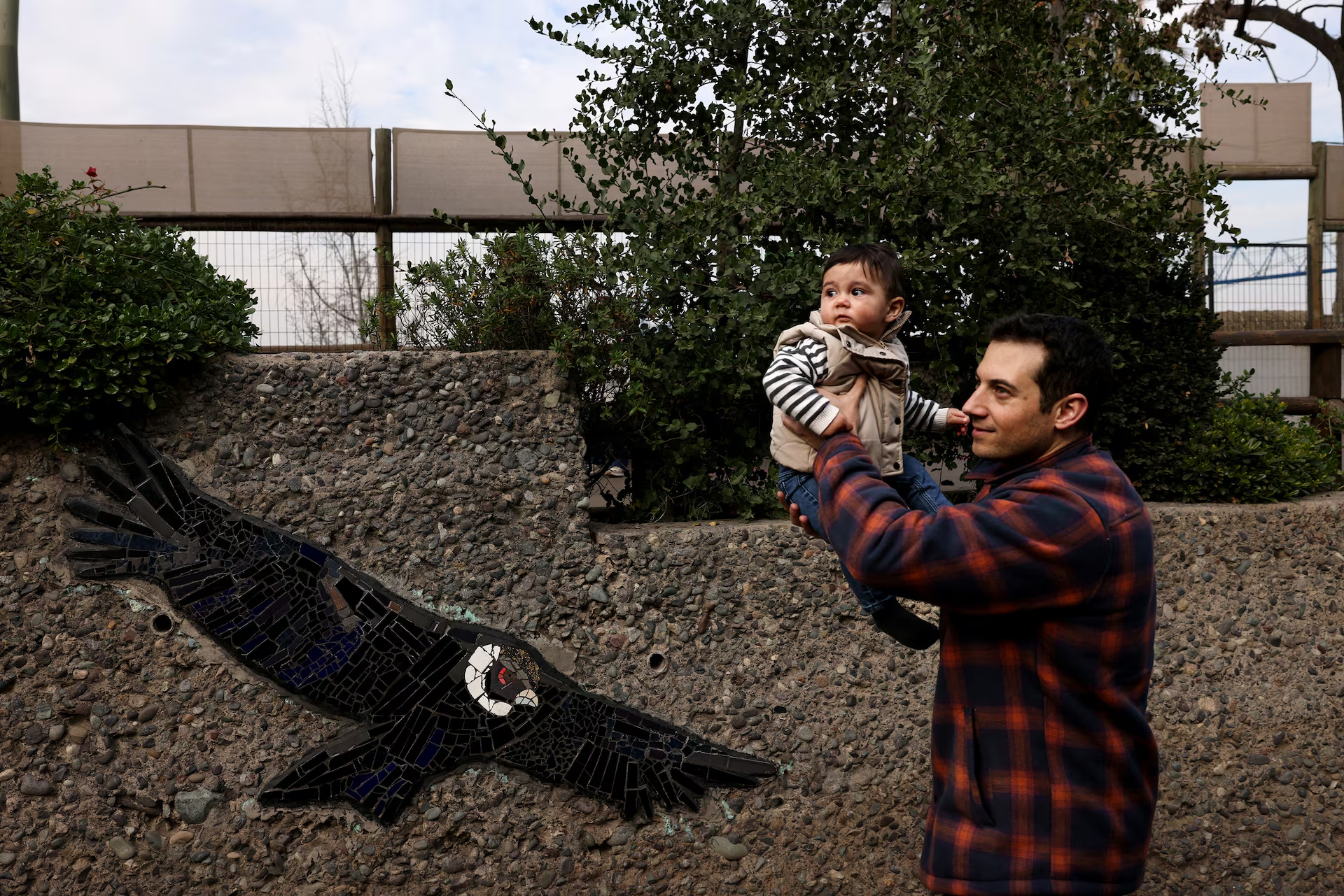 Một người đàn ông bế em bé đi ngang qua một bức tranh khảm một con thần ưng Andes ở Vườn thú Quốc gia ở Santiago, Chile. Ảnh chụp ngày 19/7. Nguồn: Reuters. Một người đàn ông bế em bé đi ngang qua một bức tranh khảm một con thần ưng Andes ở Vườn thú Quốc gia ở Santiago, Chile. Ảnh chụp ngày 19/7. Nguồn: Reuters.