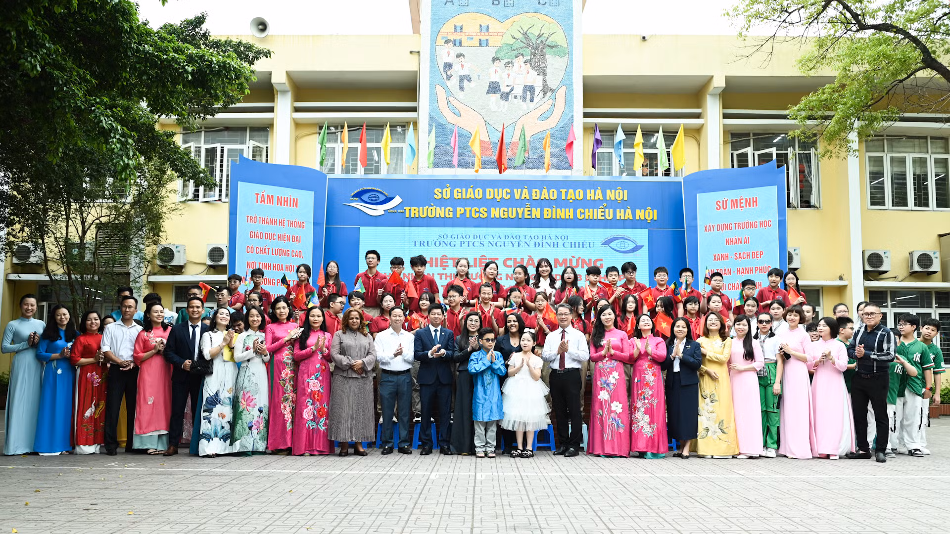 Hai Phu nhân chụp ảnh lưu niệm tại sân trường cùng Ban Giám hiệu và các em học sinh Trường phổ thông cơ sở Nguyễn Đình Chiểu.