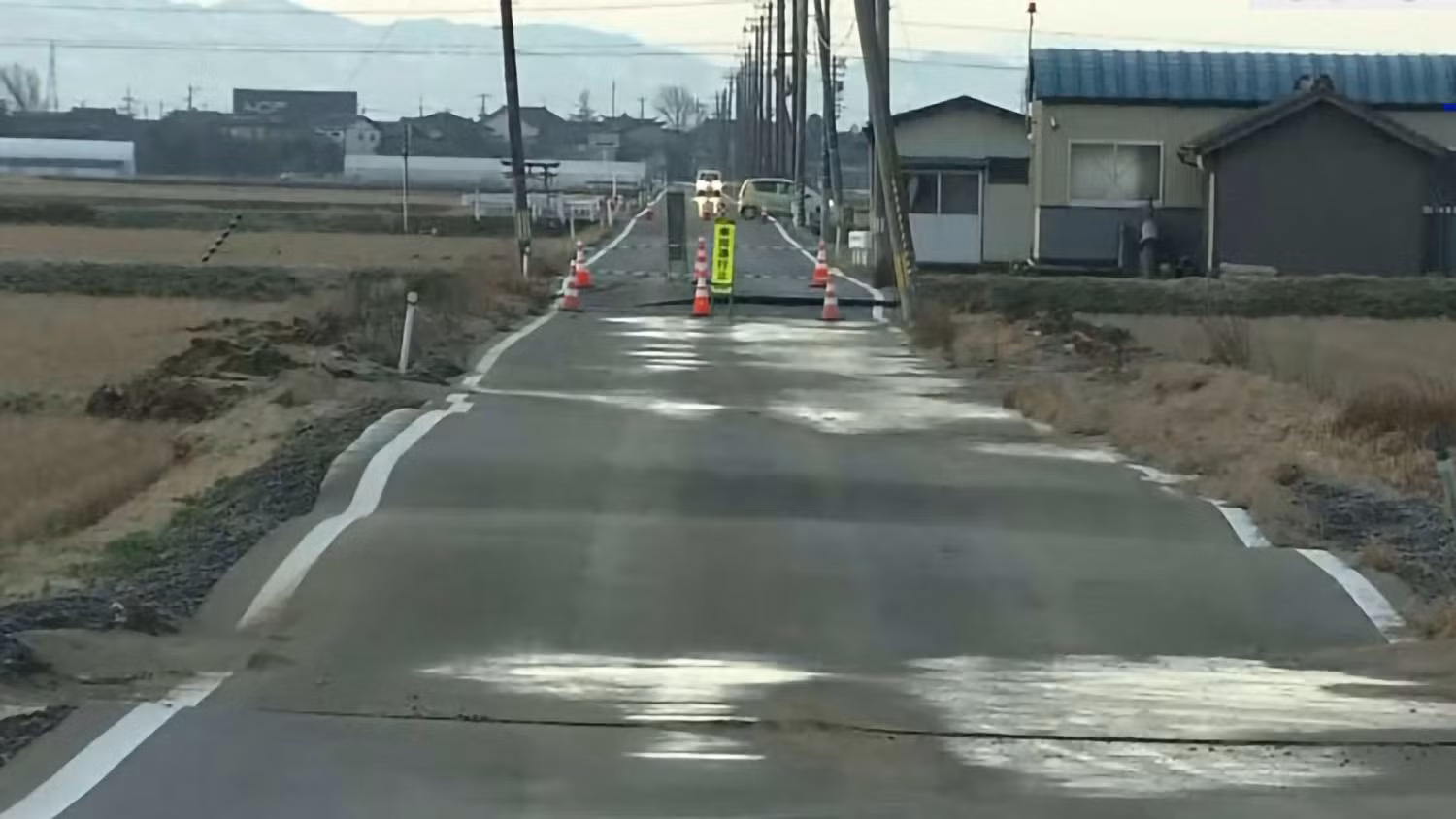 Con đường chạy qua cánh đồng lúa ở vùng nông thôn thuộc phường Nishikan, thành phố Niigata, tỉnh Niigata đã bị cấm lưu thông sau khi có vết nứt khiến mặt đường không bằng phẳng. Một số cột điện bị nghiêng hoặc đổ xuống đường. Ảnh: NHK