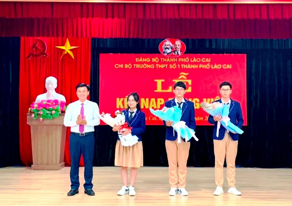 Đồng chí Đoàn Ngọc Tuyến, Phó Bí thư Thường trực Thành ủy Lào Cai tặng hoa chúc mừng ba đảng viên mới được kết nạp, là học sinh lớp 12 của Trường THPT số 1 thành phố Lào Cai. (Ảnh: Quốc Hồng)