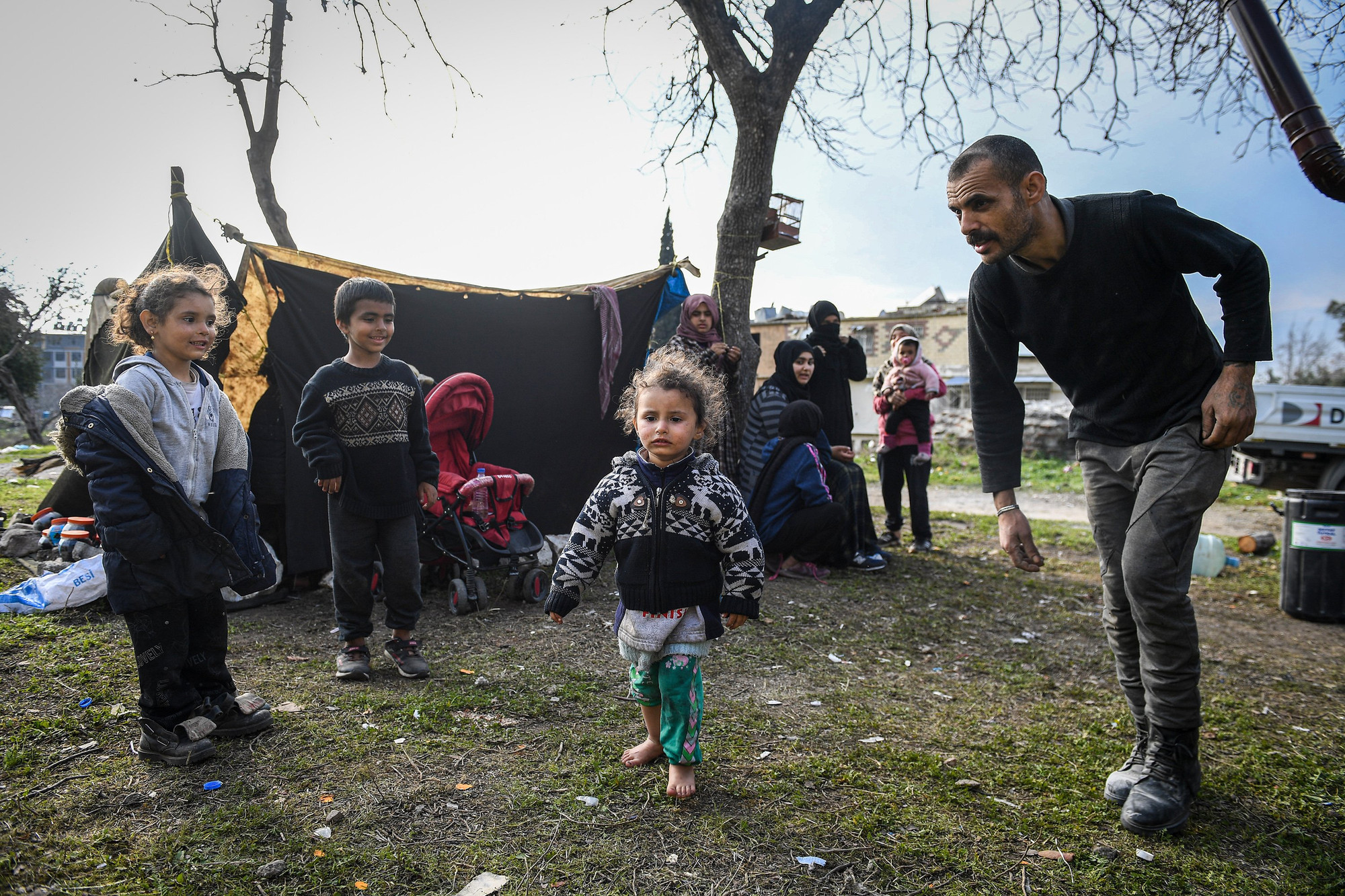 Eyhem (bên trái) ở trong 1 chiếc lều tạm rộng chừng 30m2 cùng hơn 20 người khác. Sau động đất, công việc chính của cô bé người Syria là... trông em.